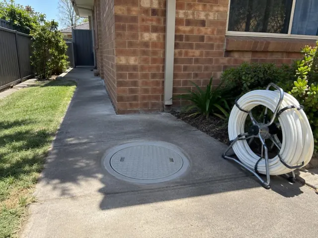 Flush round access cover in a concrete side path beside a brick house in Carramar